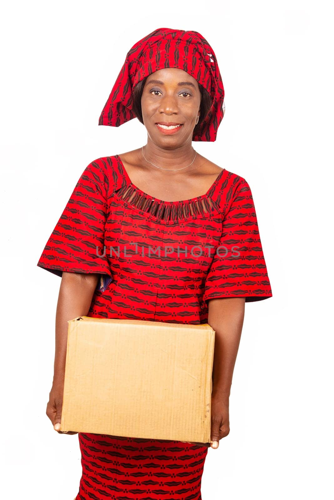 beautiful African mature woman standing and dressed in red loincloth suit holding a cardboard box in hand while being happy. White background