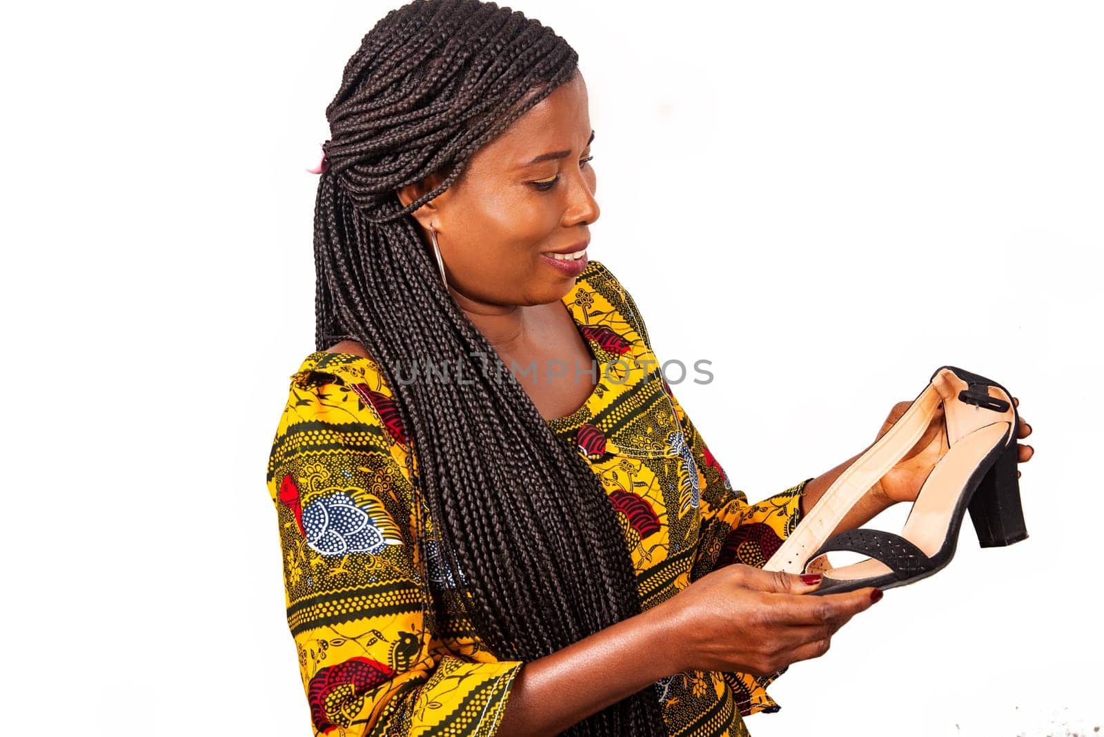 beautiful african adult woman standing with long braided hair is looking at shiny black shoes in her hand