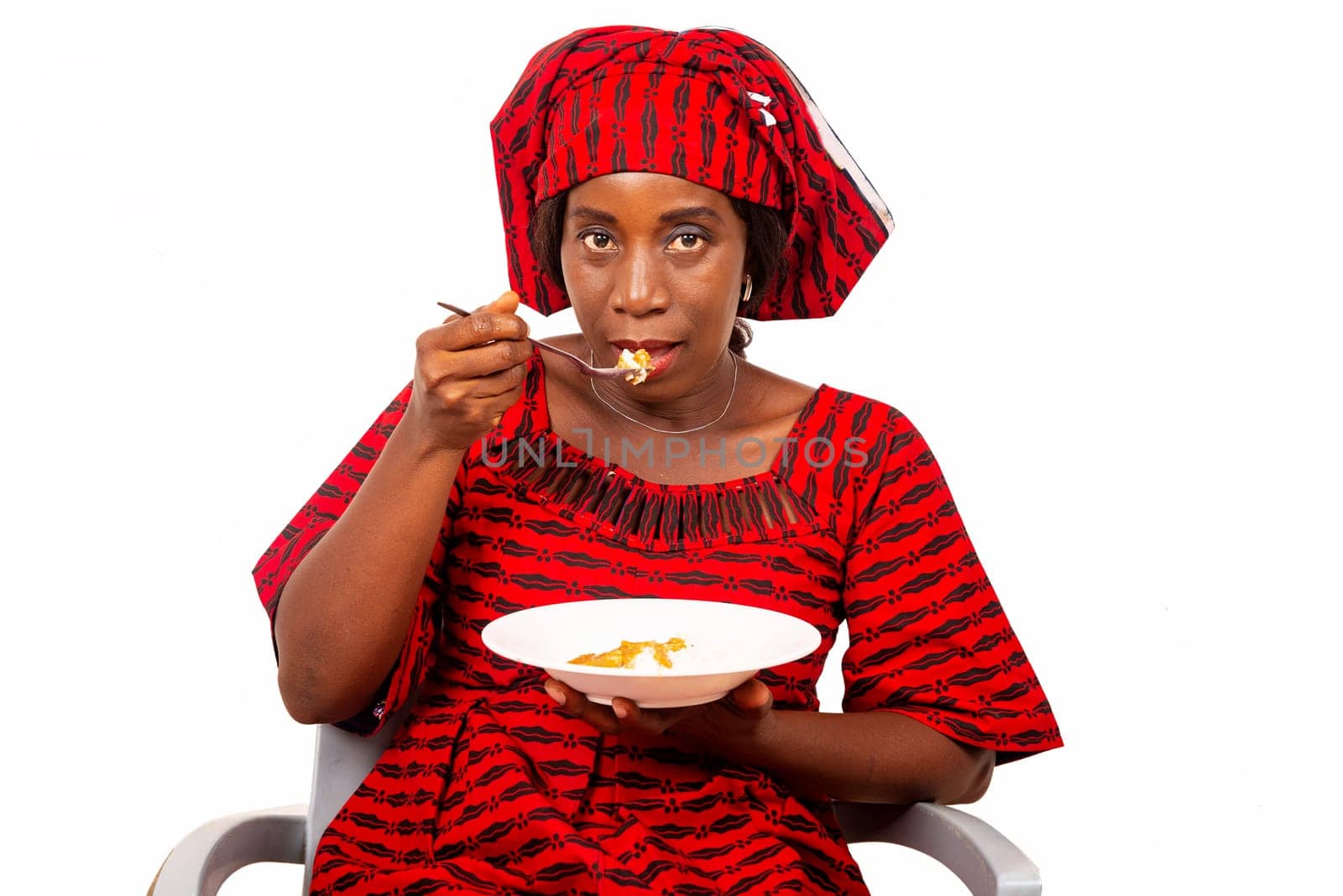 beautiful adult woman wearing red loincloth is sitting on a chair ready to eat an African meal while being smiling