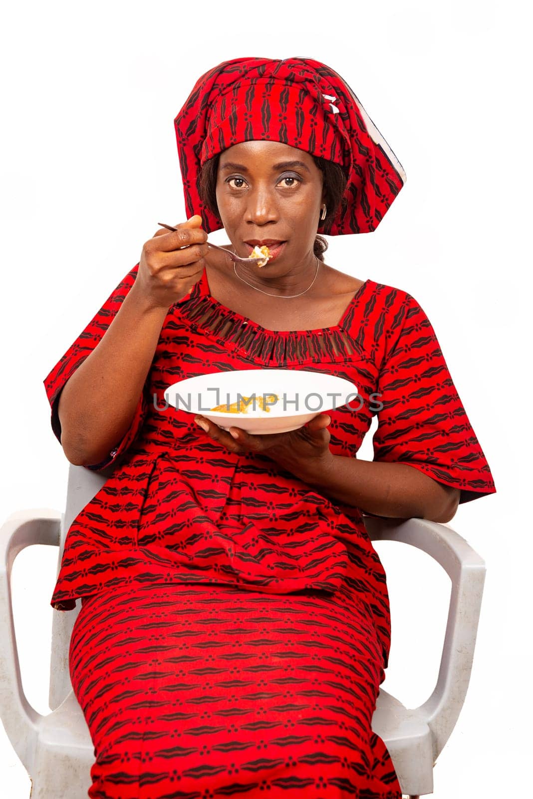 beautiful adult woman wearing red loincloth is sitting on a chair ready to eat an African meal while being smiling
