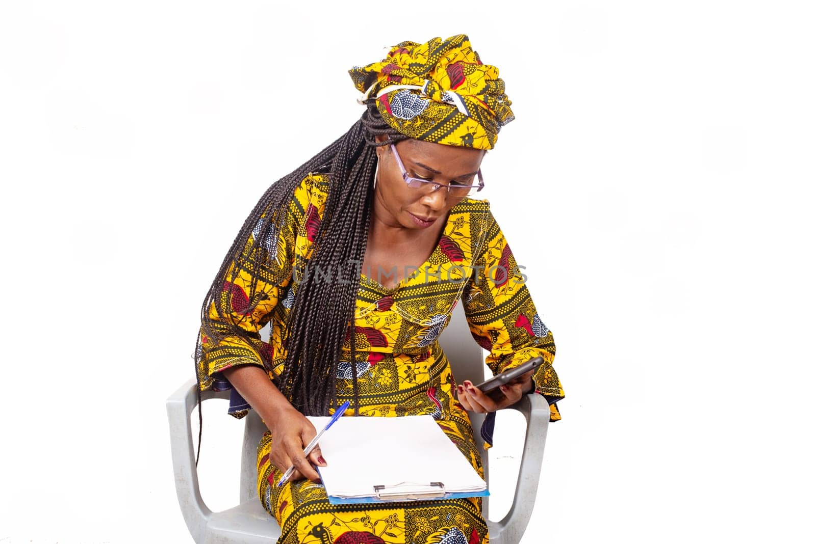 African adult woman sitting looking at a mobile phone while working and writing in a notebook