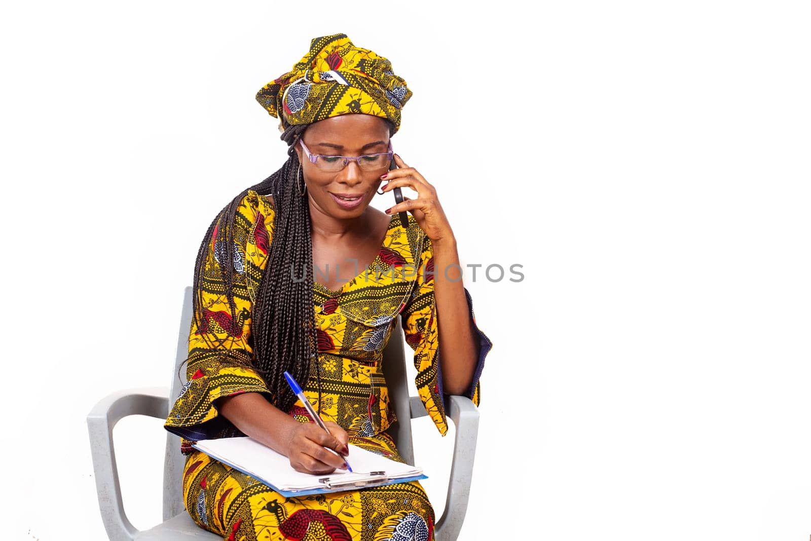 adult businesswoman sitting smiling and talking on the phone while writing in the notebook