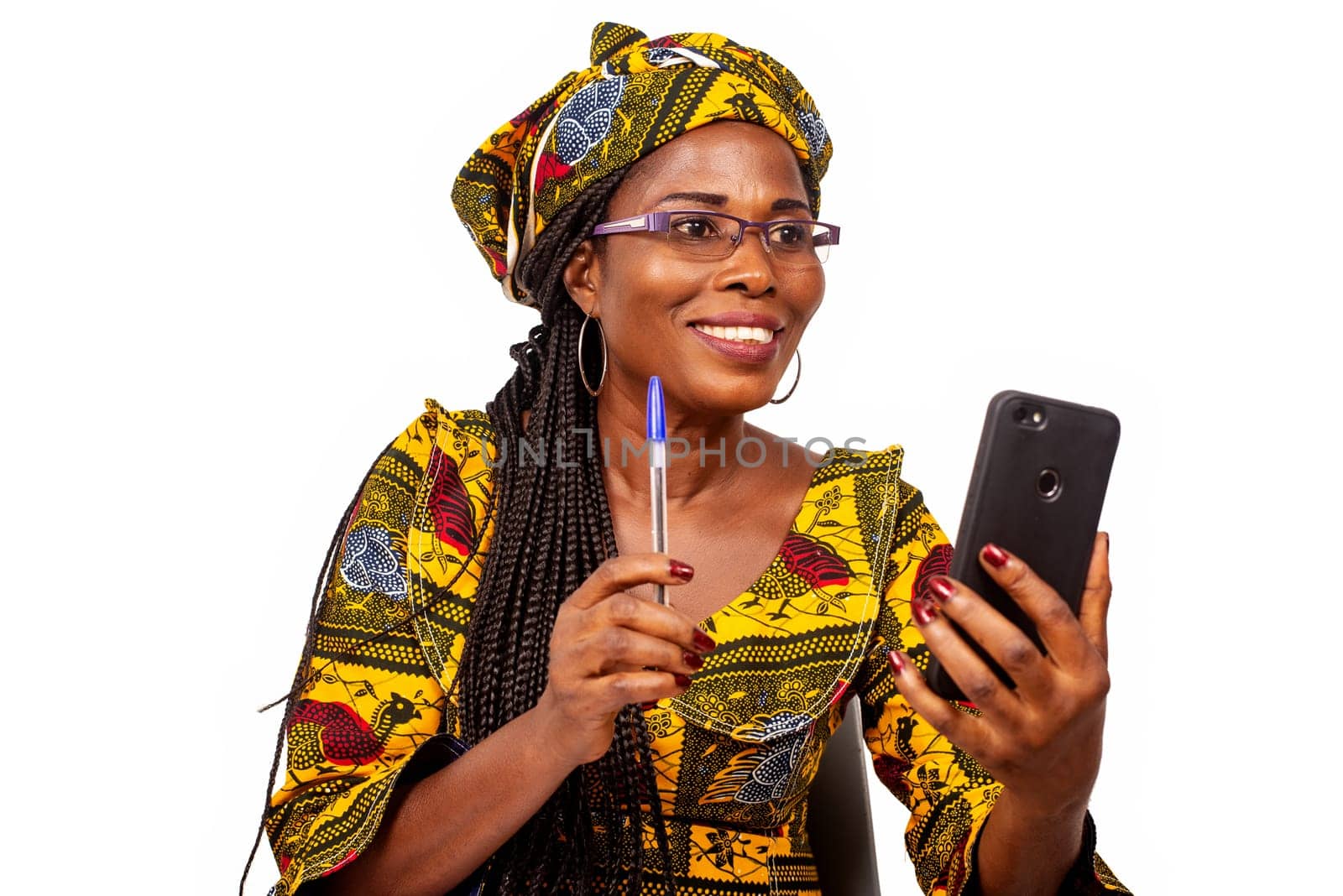 happy beautiful african mature woman sitting making a video call in her mobile telepone holding her pen in hand