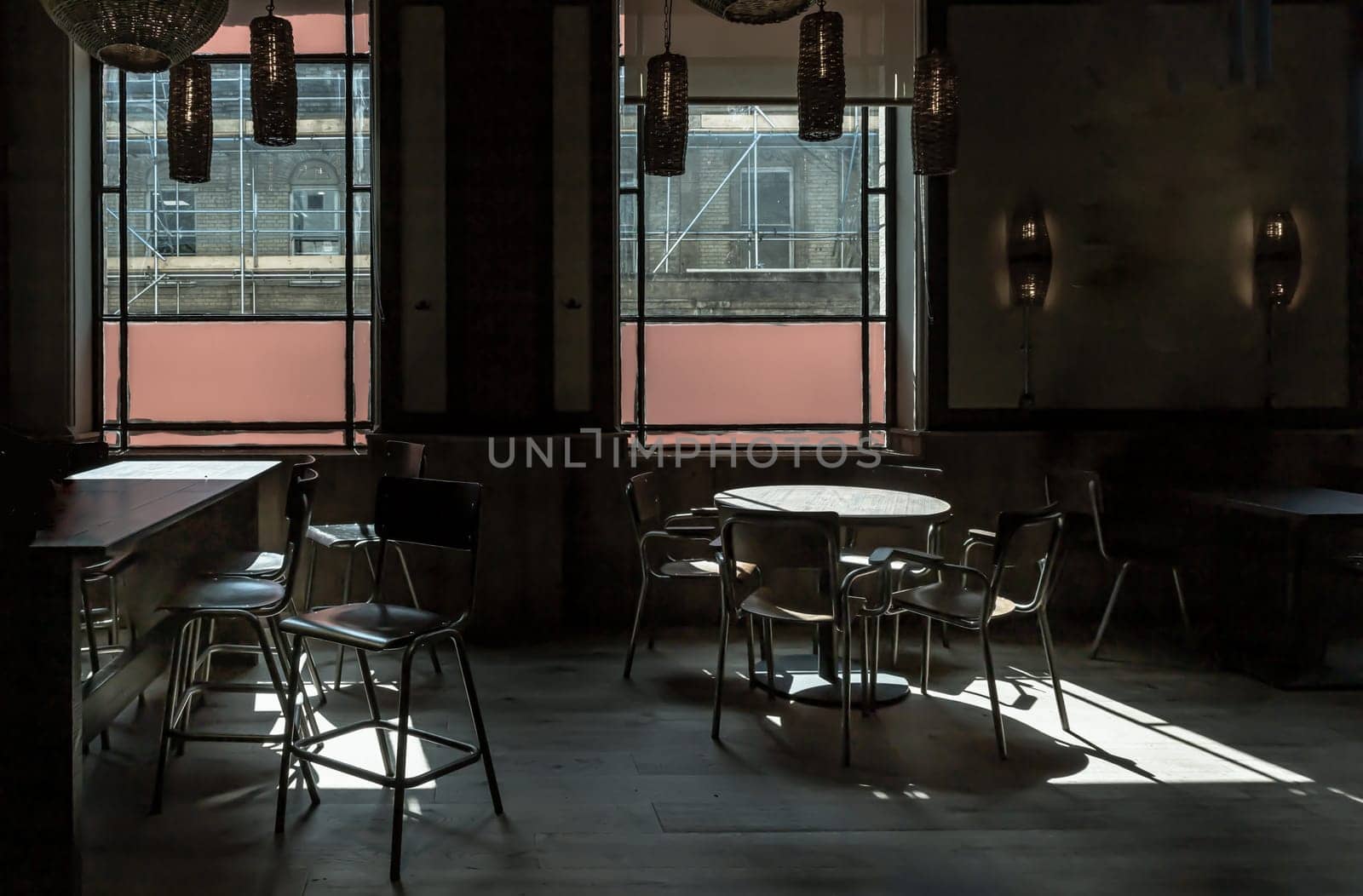 Royal Tunbridge Wells, UK - Apr 29, 2025 - Table at a restaurant with sunlight coming in through the Large windows, casting light and shadow patterns on the floor, wooden dining tables and chairs, surrounded by dark shadows inside empty room. use it as your Wallpaper, Poster and Copy space, Selective focus.