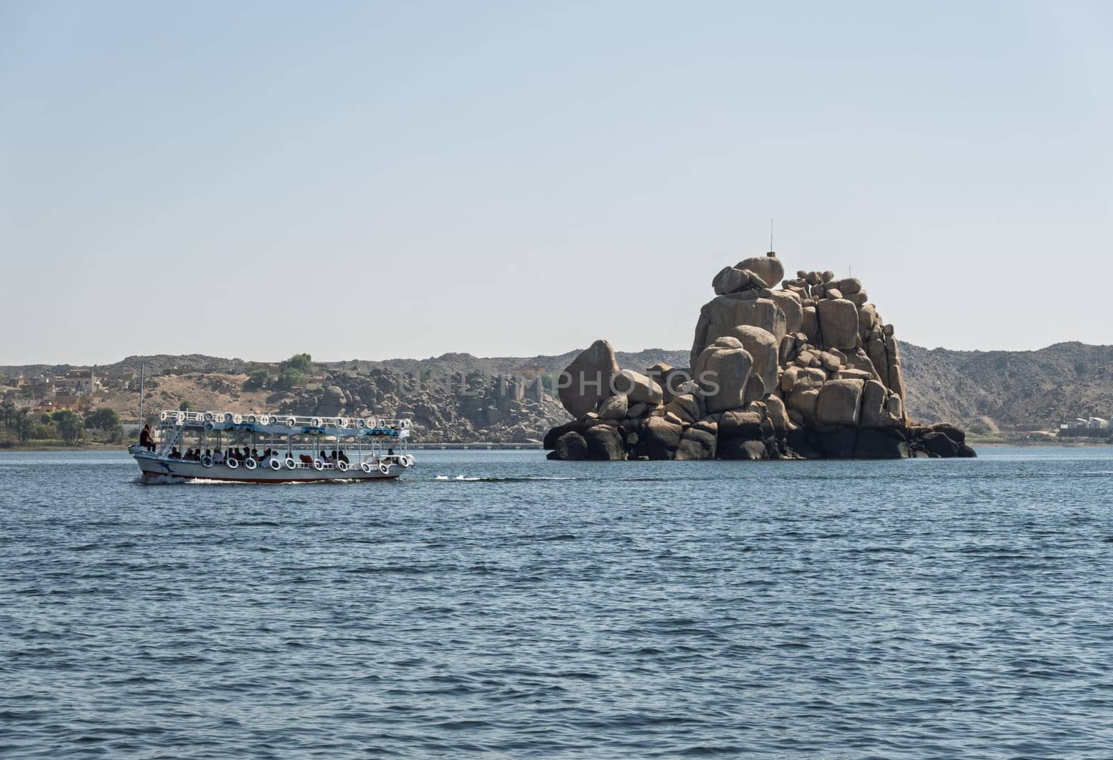 Tourists in ferry boat passing rocky island on way to Philae Temple in Aswan reservoir
