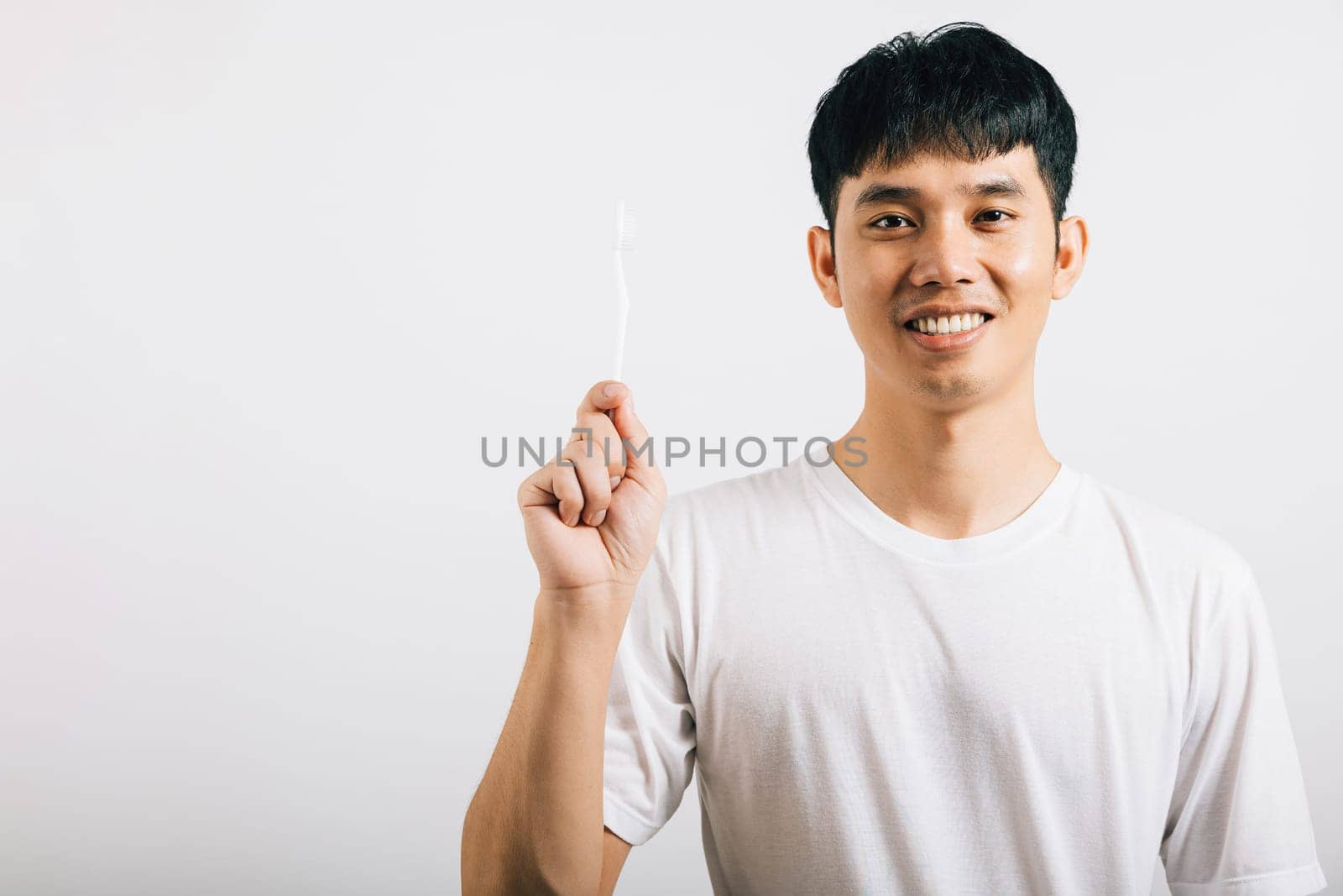 A confident Thai teenager brushes his teeth with a smile, highlighting dental health. Studio shot isolated on white, promoting oral hygiene and dental care.