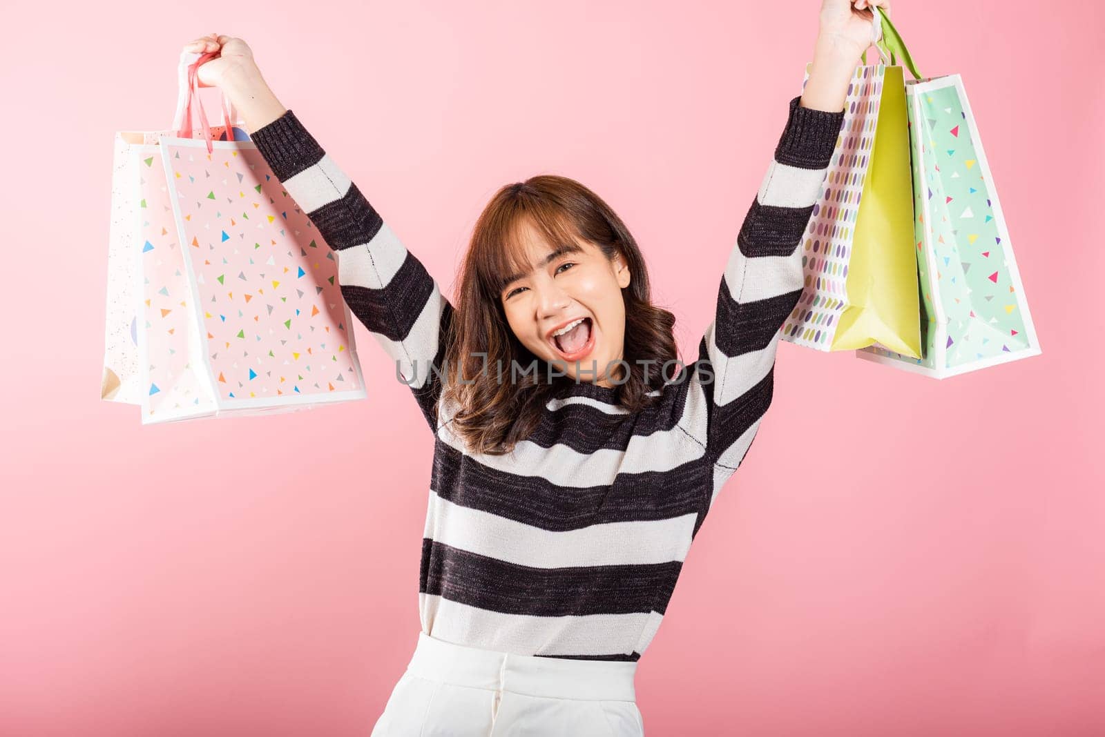 Portrait of Asian happy beautiful young woman teen shopper smiling standing excited holding online shopping bags colorful multicolor in summer, studio shot isolated on pink background with copy space