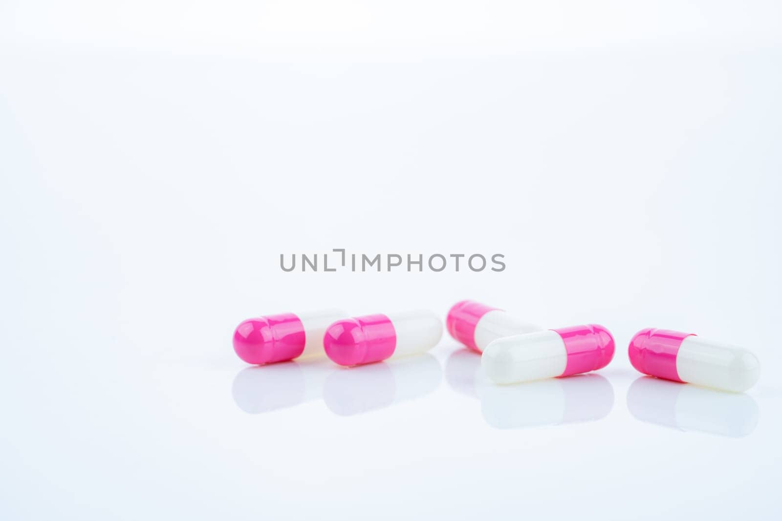 Pink-white antibiotic capsules spread on white background. Prescription drug. Antibiotic resistance in modern medicine. Healthcare and pharmaceutical industry. Medical care, pharmaceutical research.