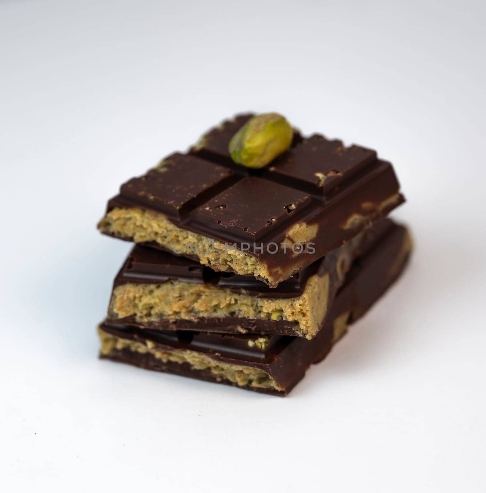 Stacked layers of kadaif embrace a generous coating of rich chocolate and are topped with a pistachio, showcasing the delightful texture and flavors in a culinary presentation.
