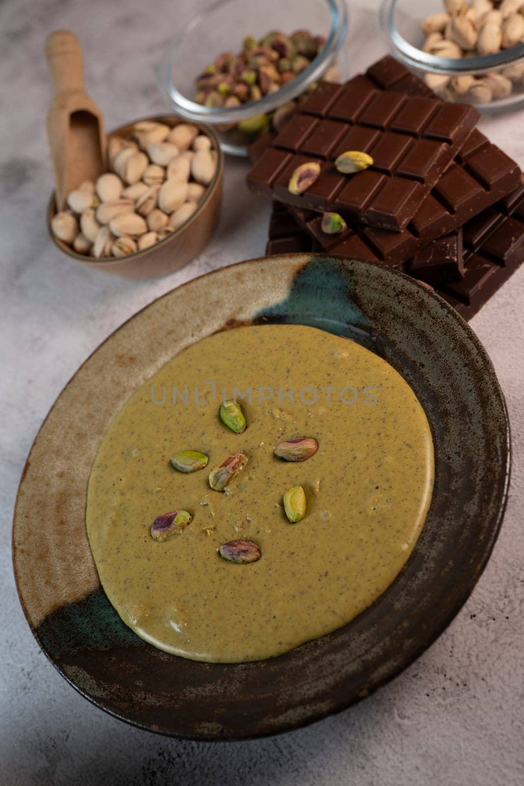 Rich pistachio cream is served in an elegant bowl, garnished with nuts, alongside chocolate pieces and additional nuts in Dubai's vibrant culinary scene.