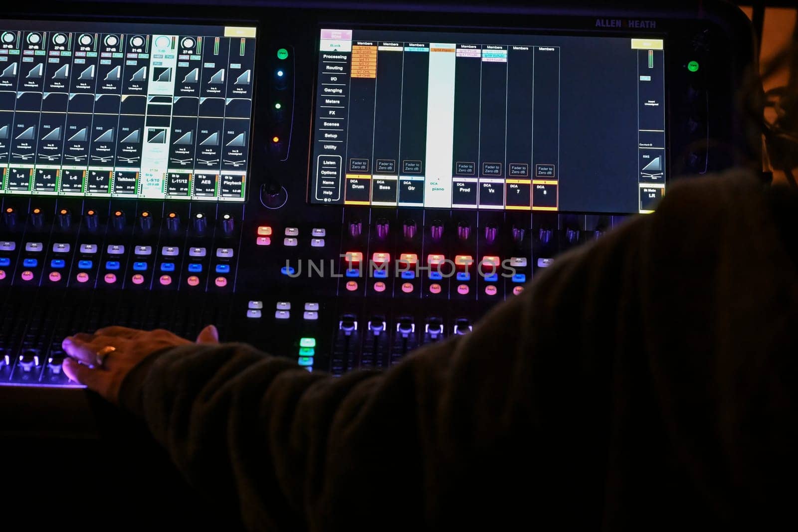 Focused sound engineer adjusts sliders and knobs on a digital mixing console while preparing for a performance in a lively venue atmosphere.