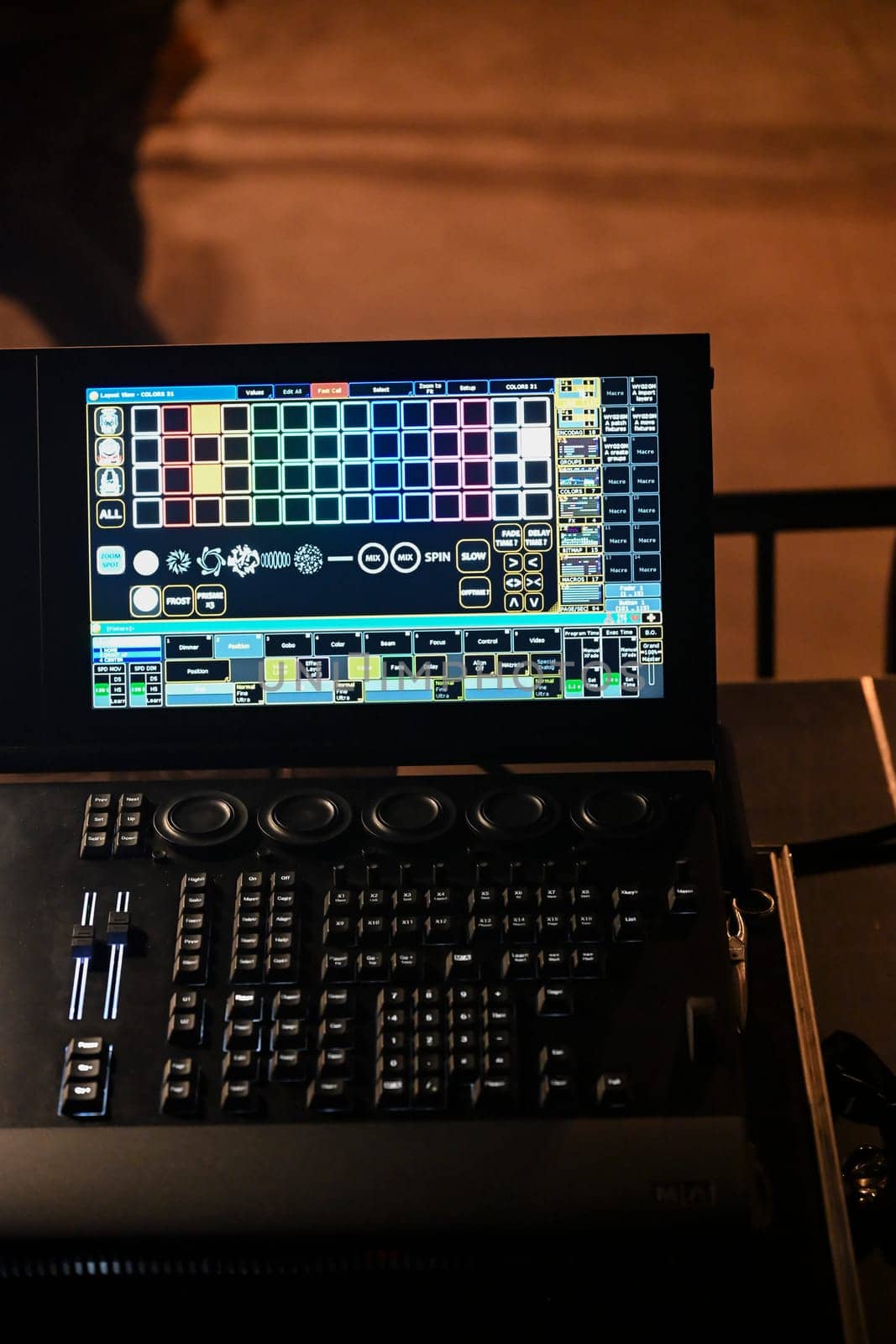 A detailed view of a lighting control panel featuring multiple digital displays and buttons, actively being used during a rehearsal at a theater venue.