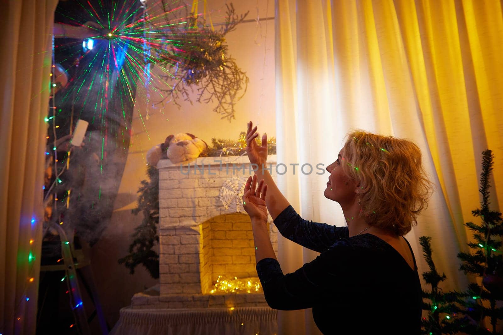 A woman joyfully interacts with colorful lights and decorations, celebrating Christmas and New Year in a festive room.