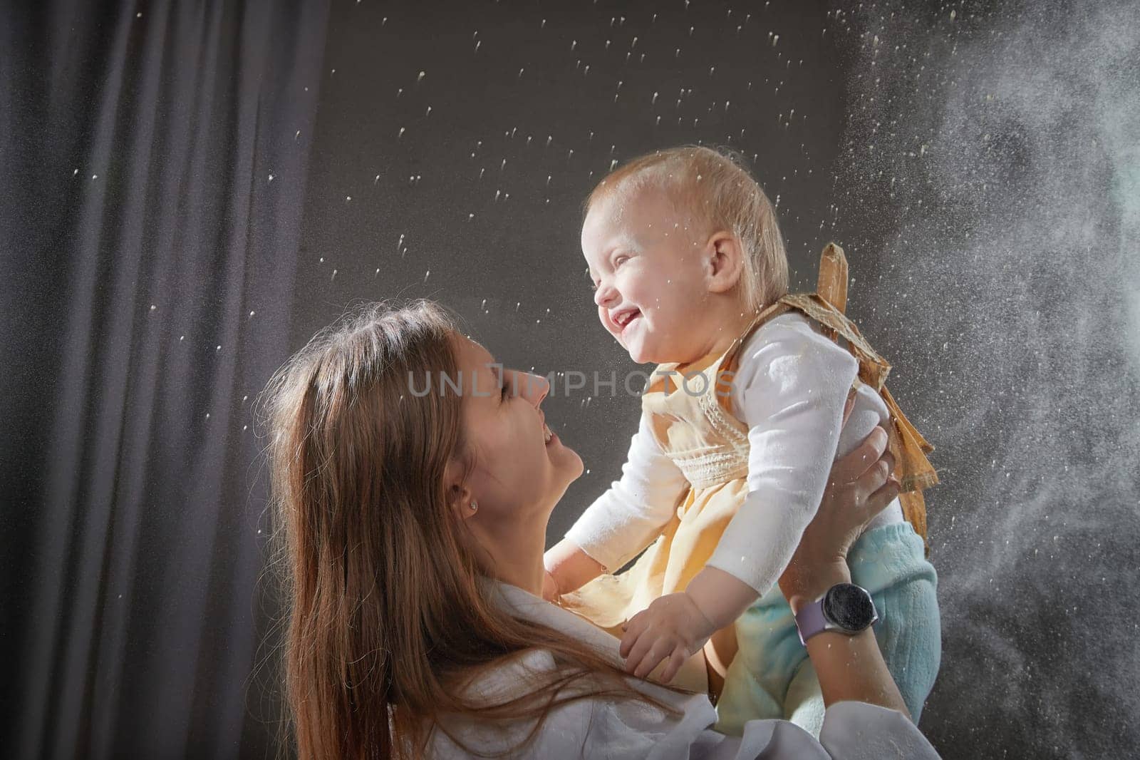 A mother and daughter joyfully engage in a flour-filled moment, creating memories in a cozy kitchen setting.