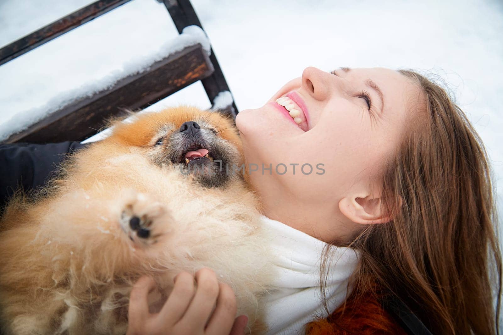 A woman joyfully interacts with her fluffy Pomeranian, surrounded by a snowy landscape in winter.