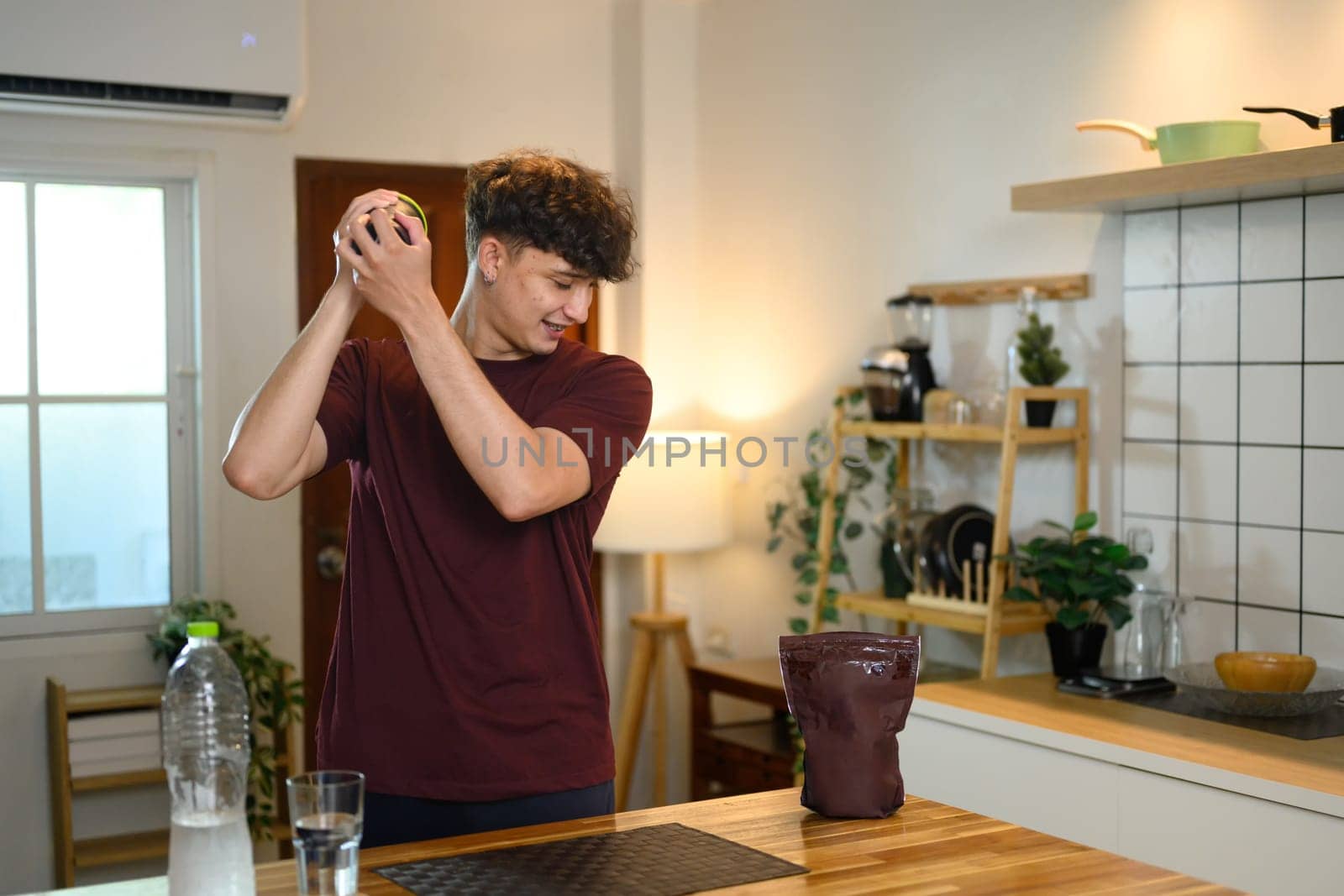 Man shaking a protein shaker bottle in a kitchen preparing nutritious fitness drink.