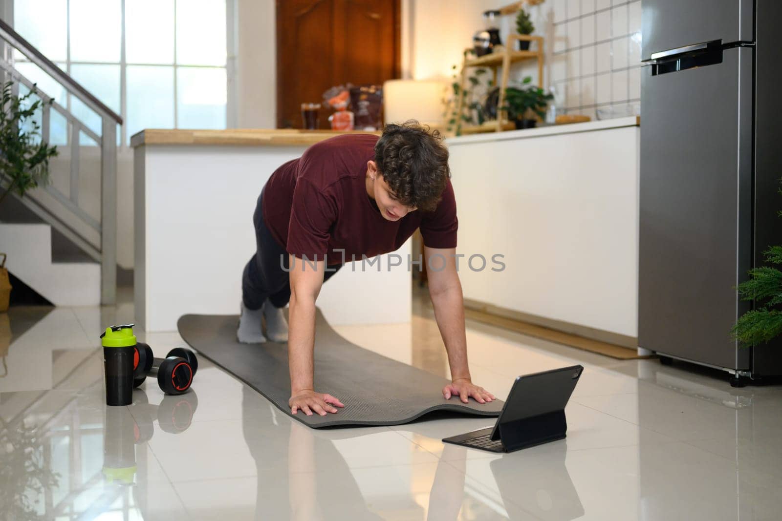 Active man doing plank exercise on mat and following an online workout on digital tablet.