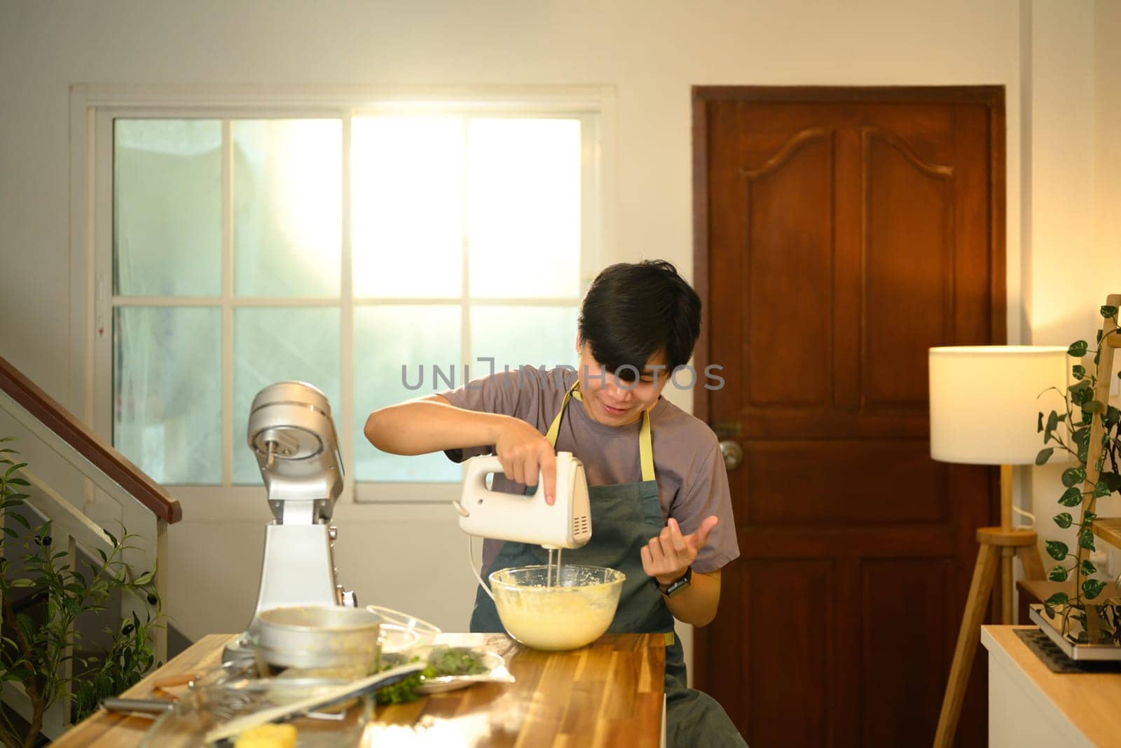 Young asian man using a hand mixer to whip ingredients for compound butter.