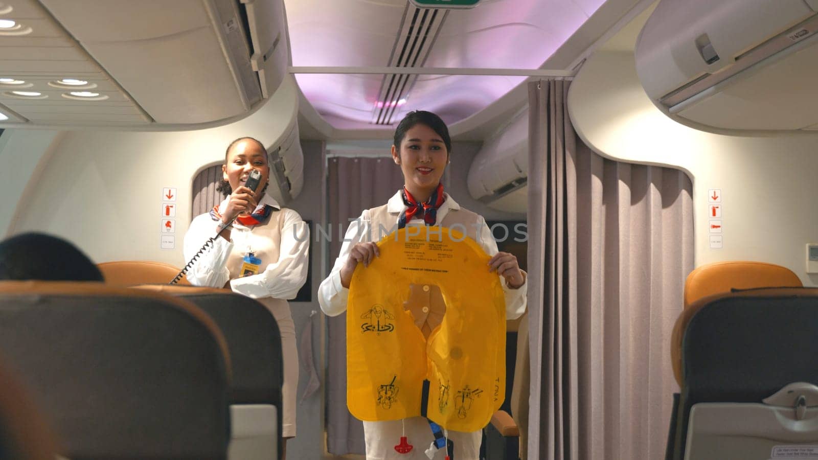 Asian stewardess safety explaining passengers prior to flight take off in airplane, air hostess uniform safety demonstration presenting pre-flight safety instructions life vest in emergency situation