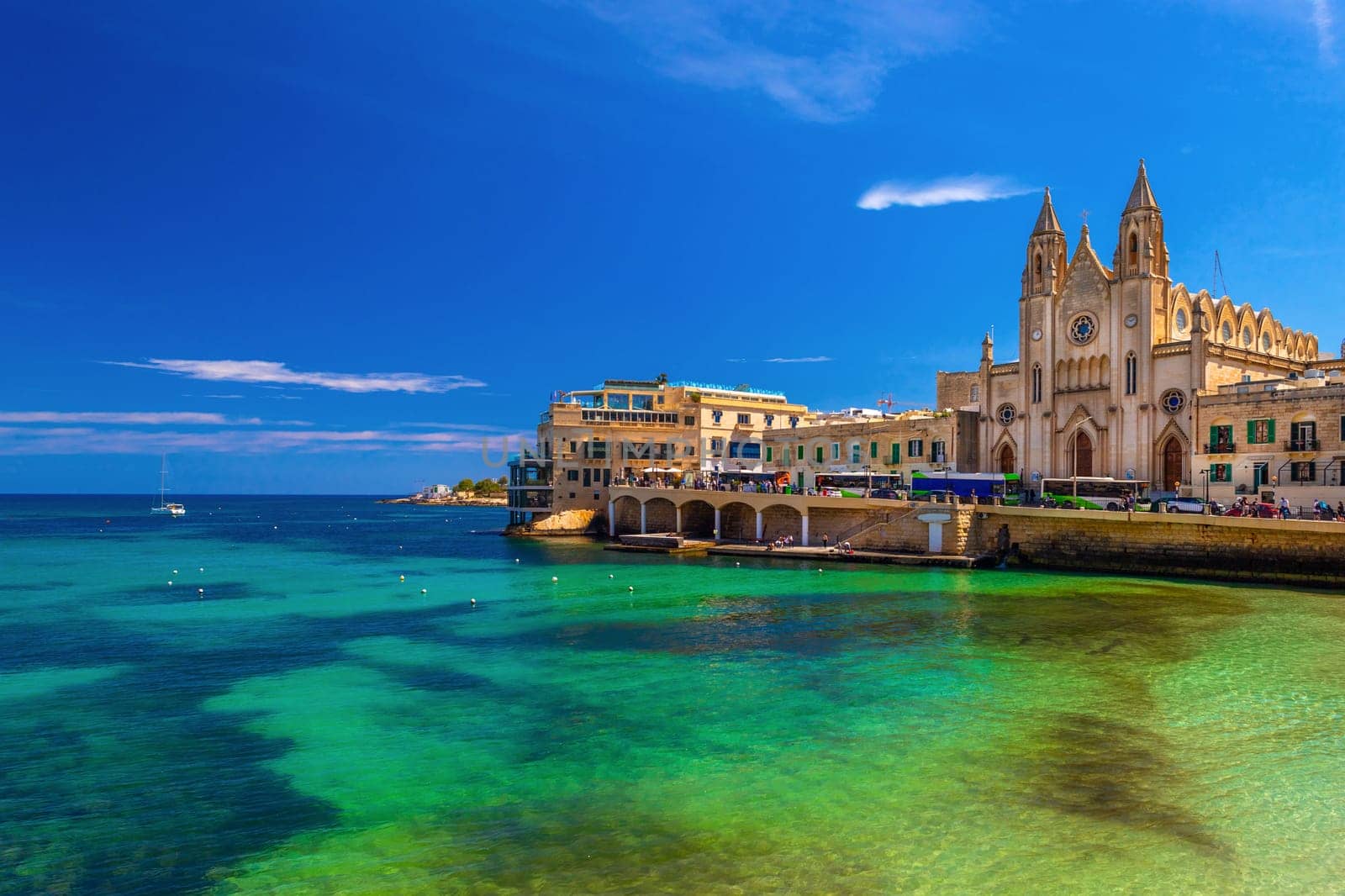Picturesque view of the Knisja tal-Karmnu and turquise-green water in St. Julian's Bay in Sliema, Malta.