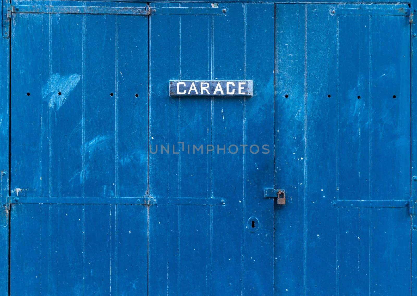 Blue wooden garage door with the inscription - Garage. Closed garage gate with a small lock on it.