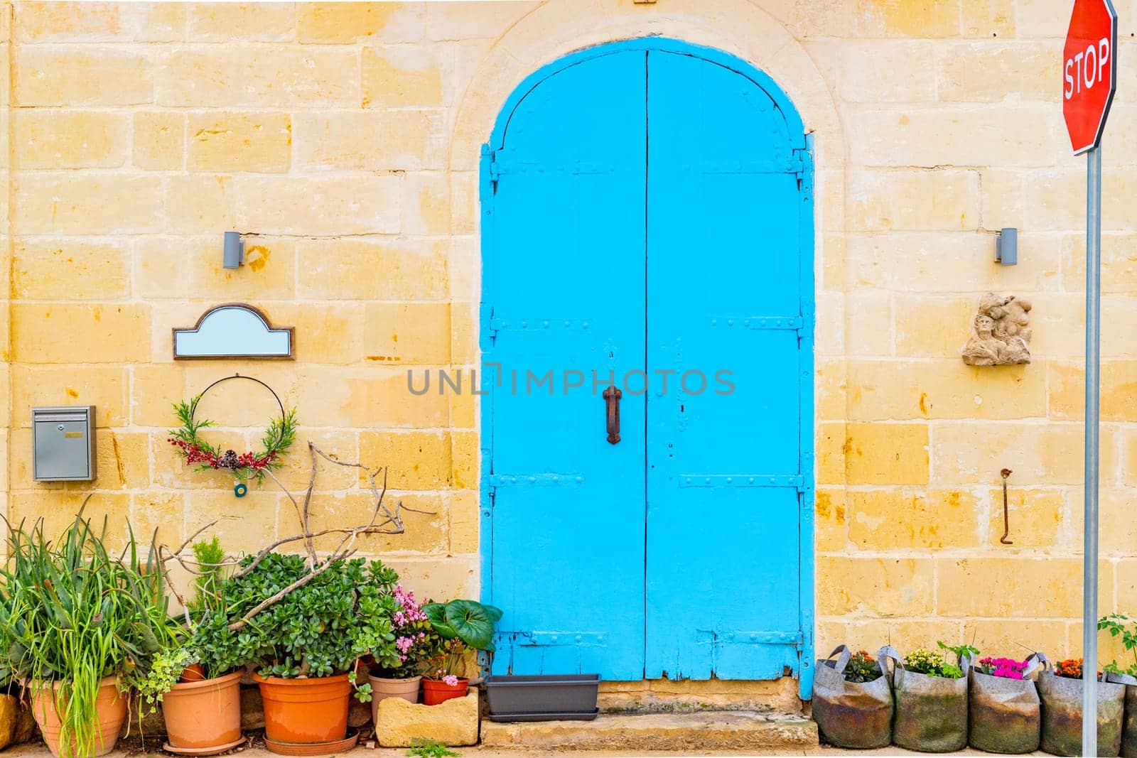 Residential building facade made of stone brick with metal door painted blue, potted plants near it and a stop traffic road sign