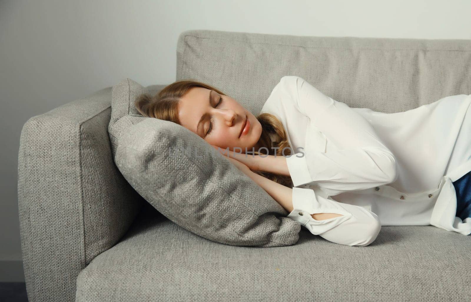 Happy relaxed young woman sleeping lying on the couch on gray soft comfortable pillow in living room at home