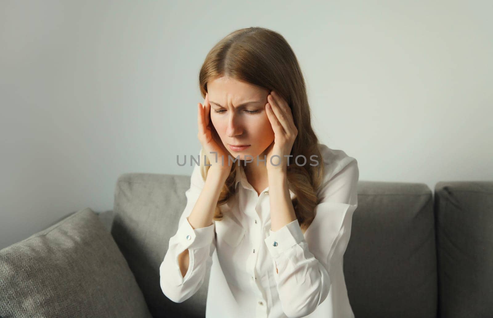 Exhausted tired woman touching head, suffering from headache, stress, fatigue, temples pain, migraine, loud noise, tension sitting on the couch at home