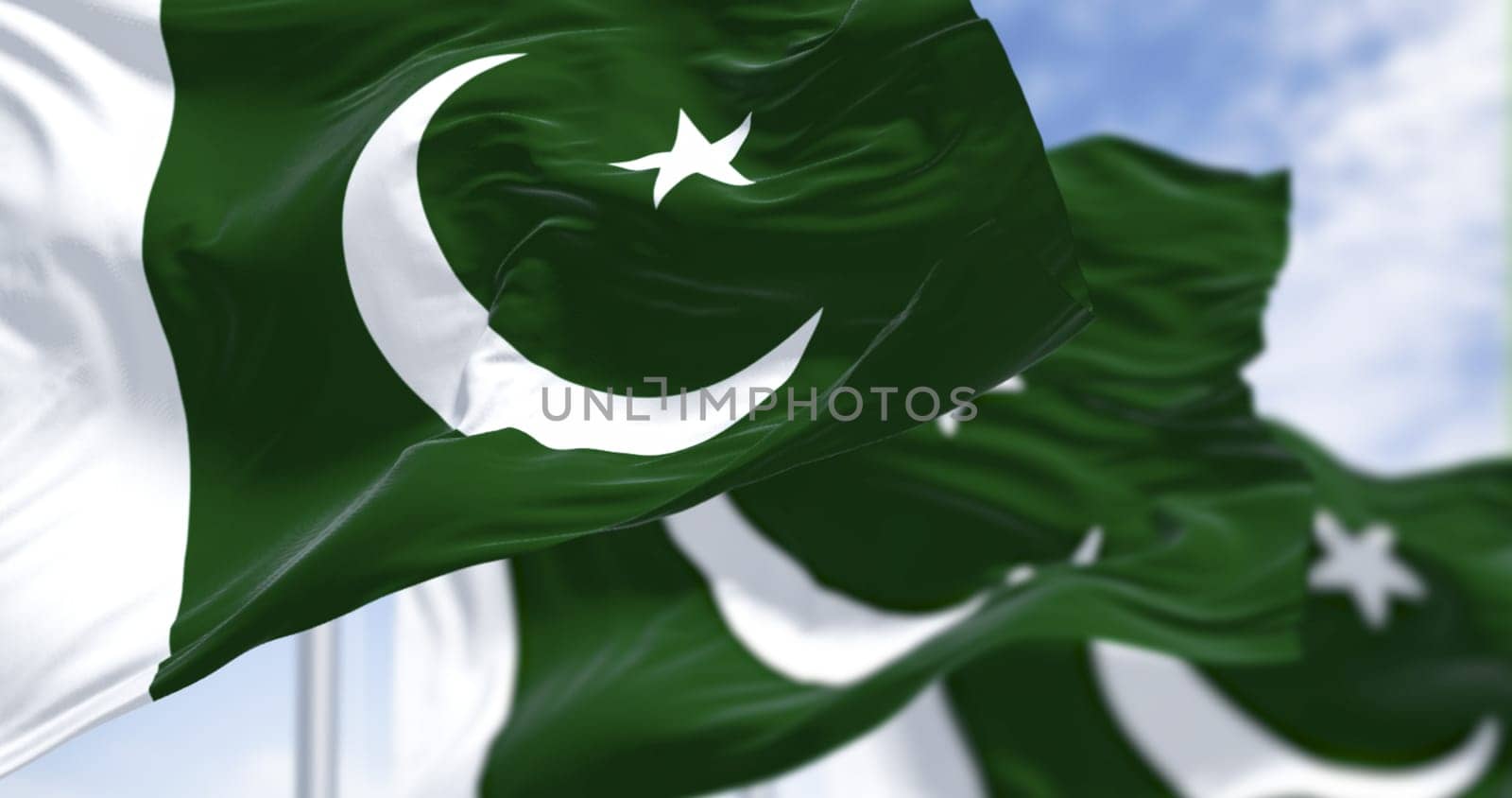 Close-up of Pakistan flags with crescent and five-pointed star, fluttering in the wind against a blue sky, symbolizing pride, Islam, and national unity. 3D fabric render with detailed texture.