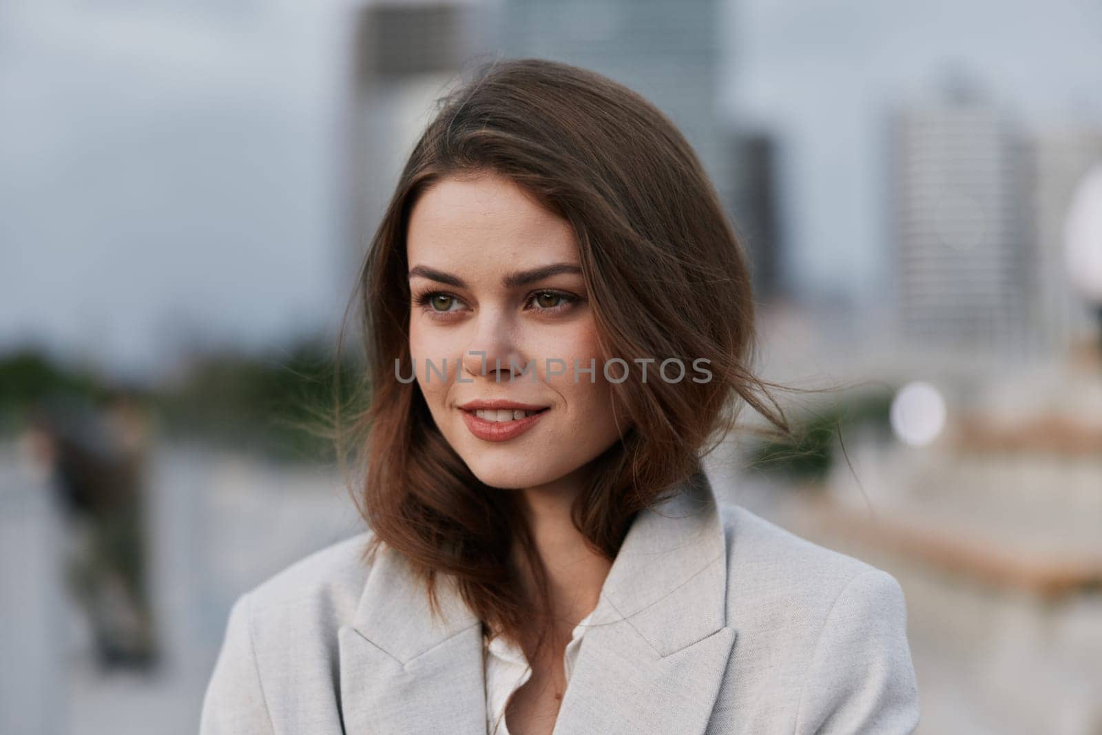 A businesswoman exudes confidence and ambition, dressed in a tailored suit with a joyful expression, set against a modern city backdrop.