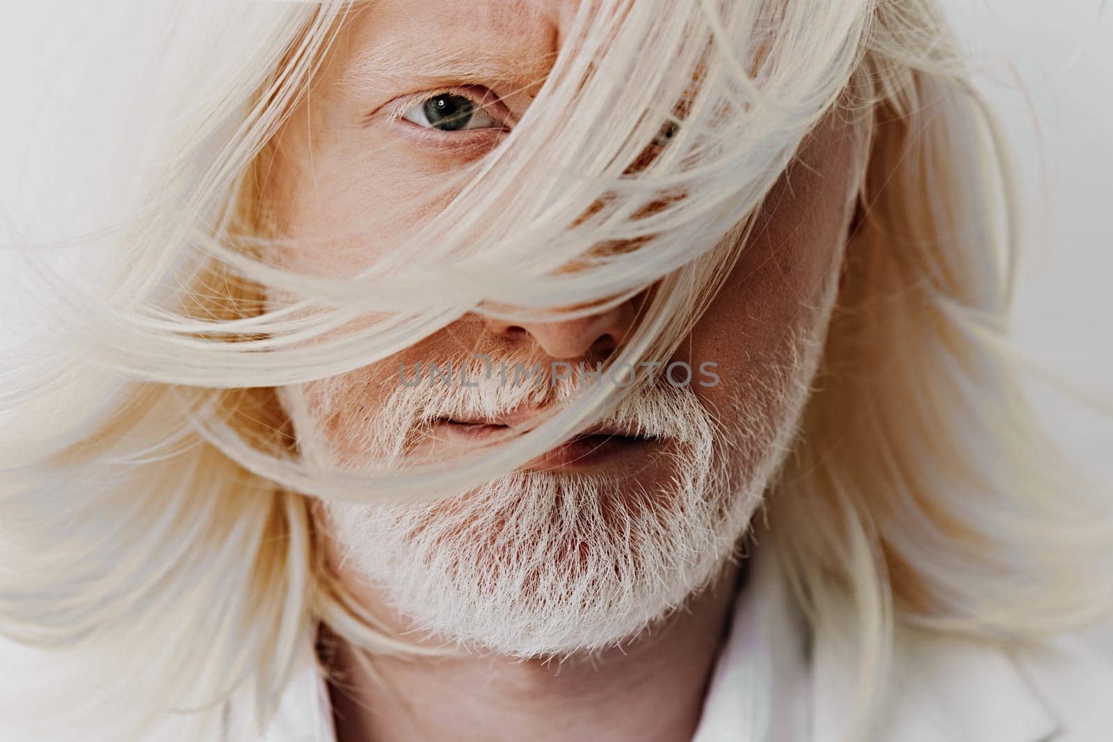 Close up portrait of an elderly man with long, flowing white hair and a beard, set against a gentle white background His piercing blue eyes convey deep emotion, with hair moving gracefully