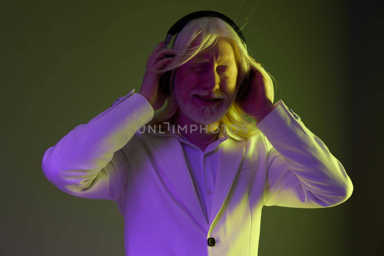 A stylish man with flowing blonde hair and a white suit is immersed in music while wearing headphones The background features a smooth gradient of purple and green, creating a modern and vibrant atmosphere