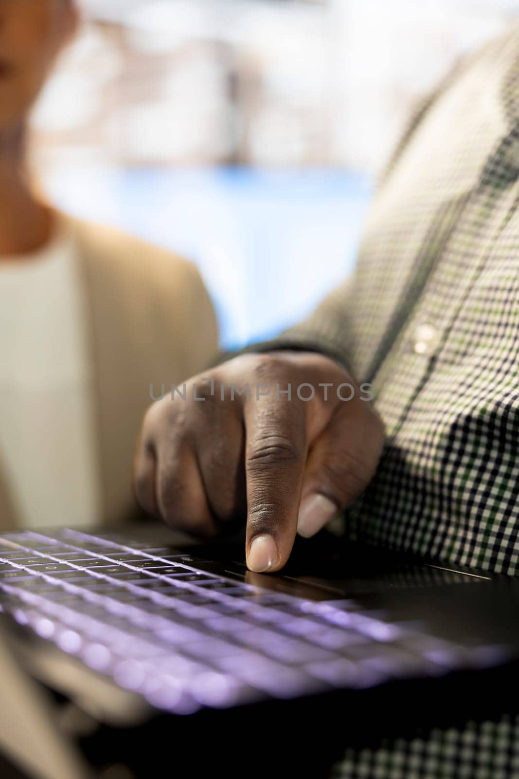 African american man next to colleagues in office coordinating company administrative operation, writing documents on notebook. Close up of employee typing on laptop keyboard, inputting data metrics