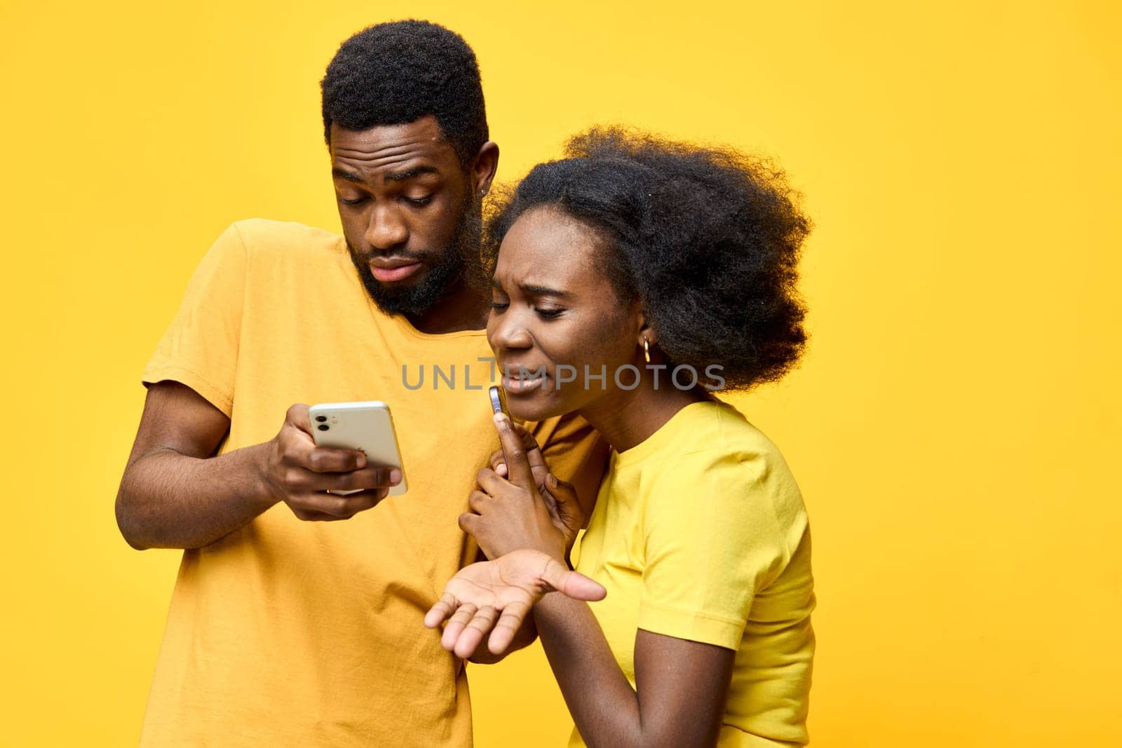 A couple in yellow attire displays emotions of frustration and concern as they check a smartphone against a vivid yellow backdrop, highlighting modern communication challenges