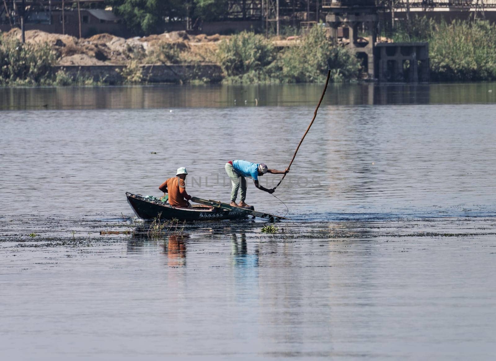 Two men in their small boat on a calm river Nile while tending to fishing net in the water