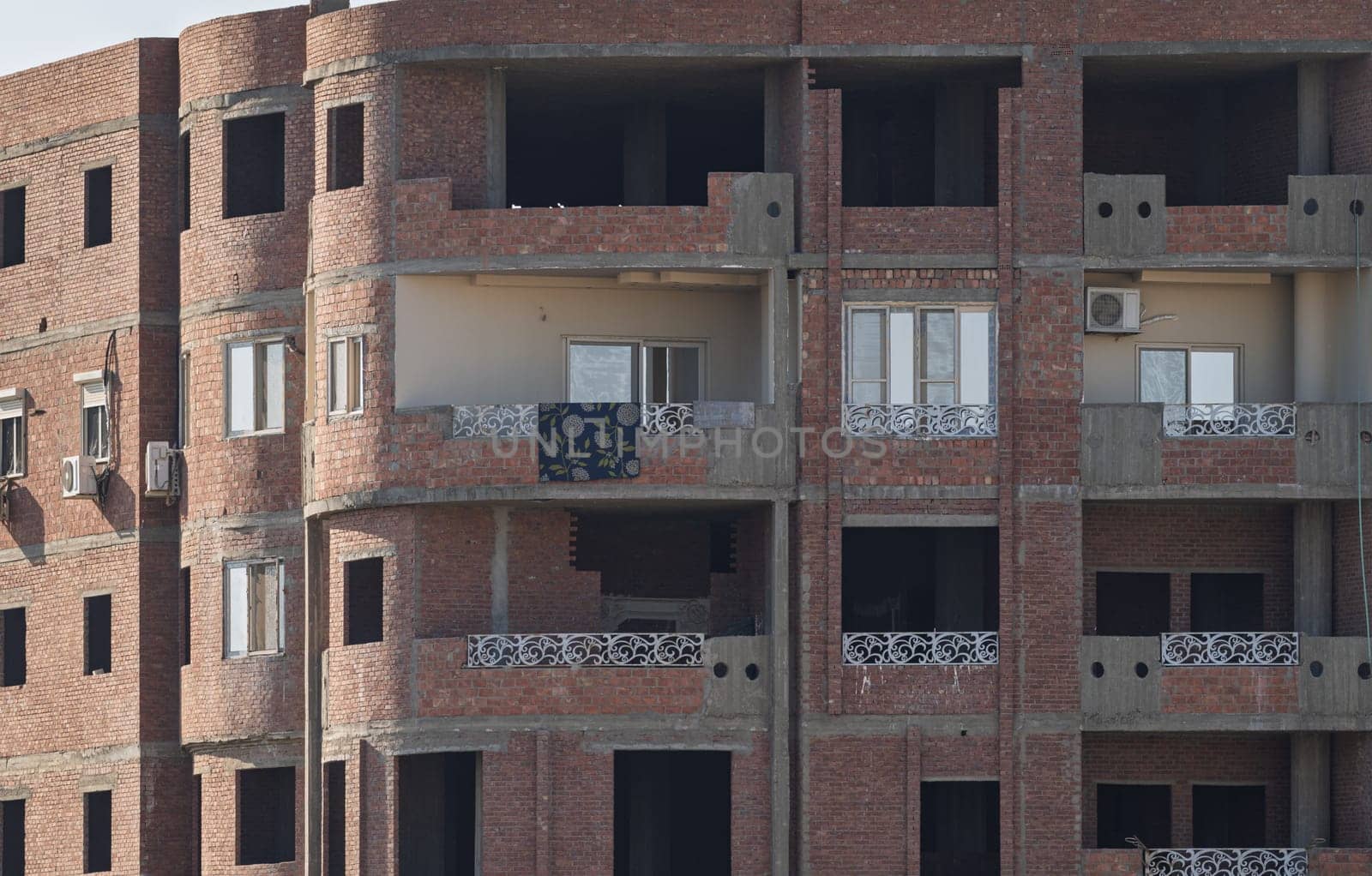 An unfinished building in Esna, Egypt, with brick and concrete construction and rebar on roof. Some apartments occupied