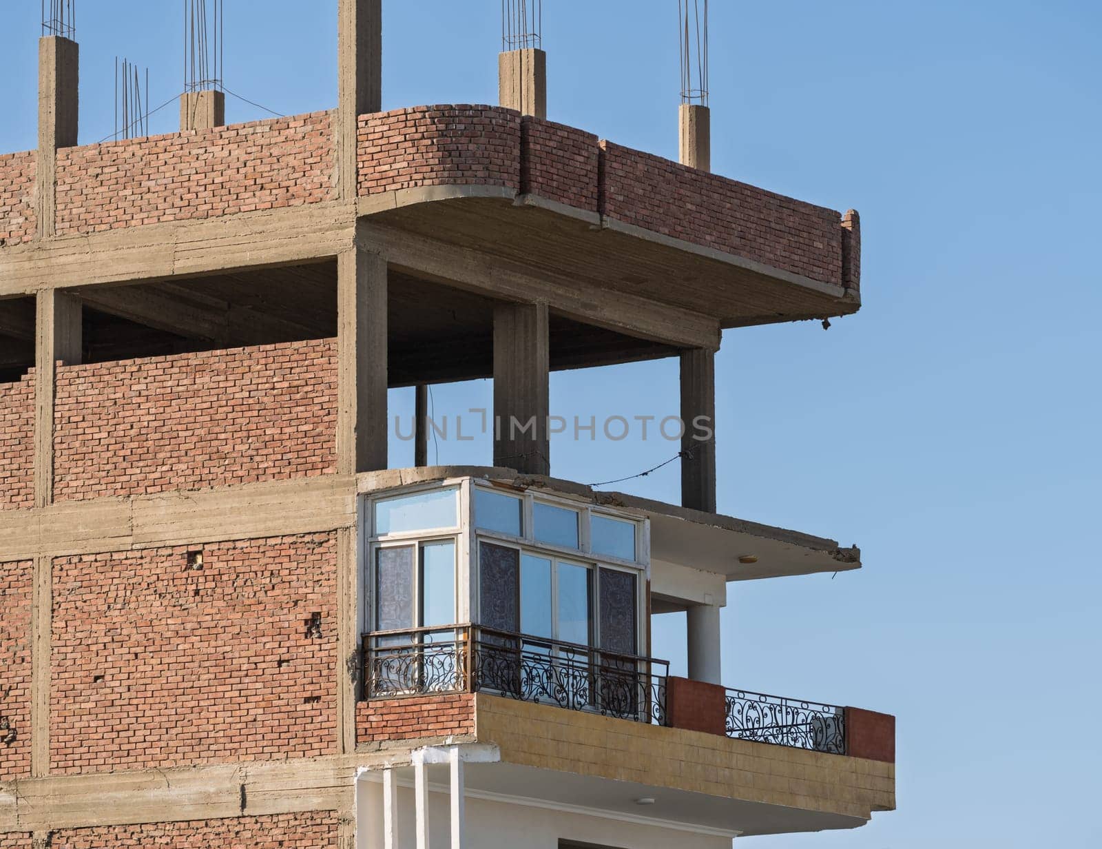 An unfinished building in Esna, Egypt, with brick and concrete construction and rebar on roof. Some apartments occupied