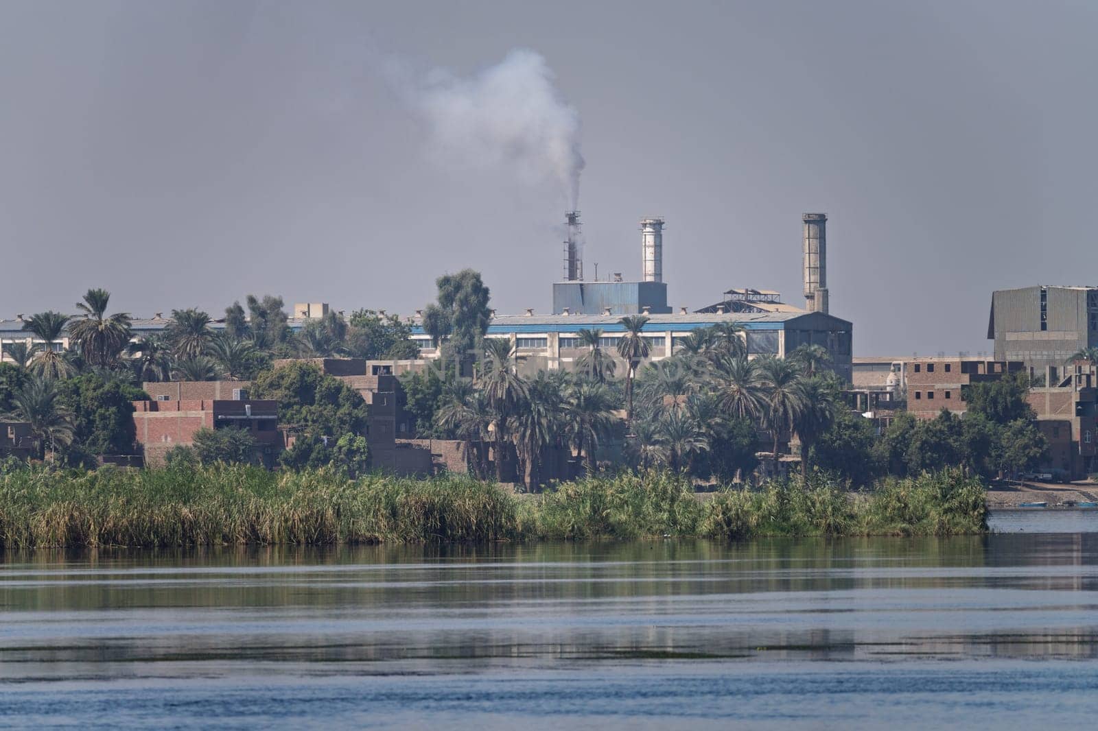 A view of the Edfu steel factory, including industrial buildings, smokestacks, seen from the Nile River
