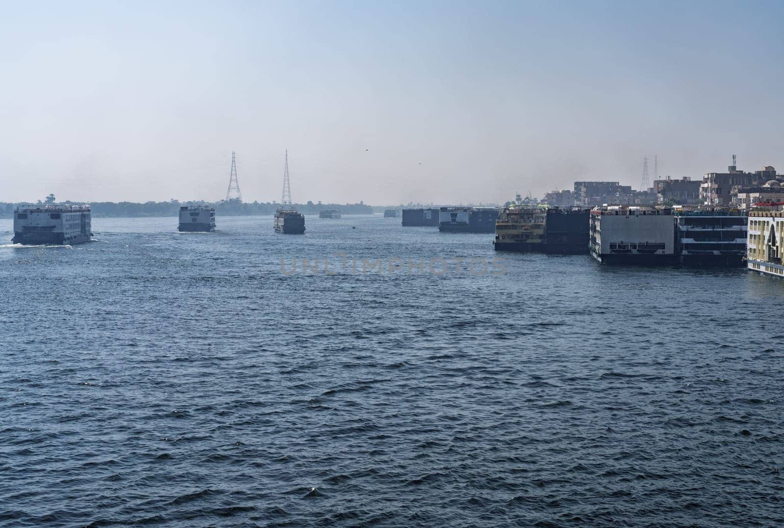 Crowded harbor in Edfu with Nile cruise boats docked and others leaving for Aswan on river in Egypt