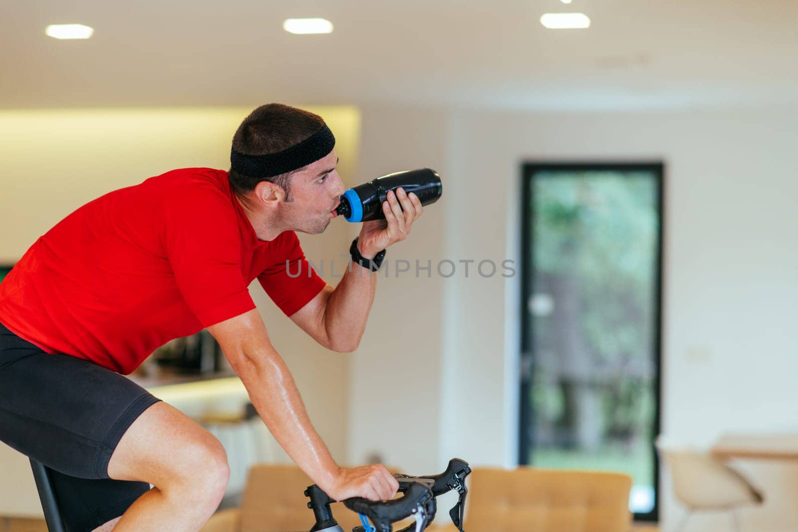 A triathlete riding a triathlon bike on a machine simulation in a modern living room. Training during pandemic conditions