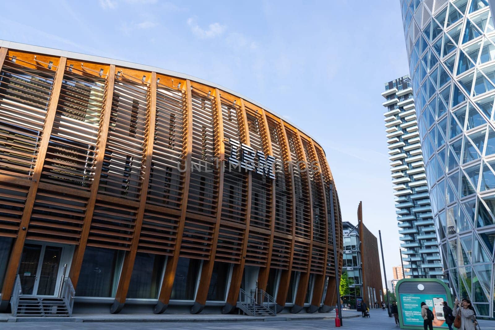 Milan, Italy - April, 08, 2025: IBM Pavilion in Milan. Modern eco-architecture with wooden slats, urban skyscrapers and pedestrians in Porta Nuova district.