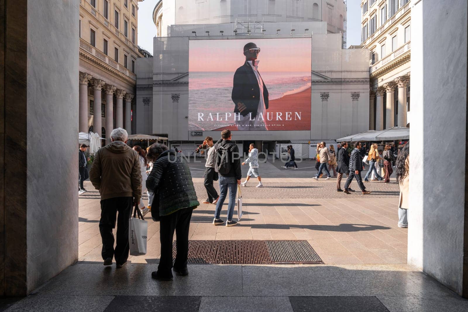 Milan, Italy - April, 08, 2025: Ralph Lauren billboard in Milan. People walking in Piazza San Babila. Large fashion advertisement on historic building.