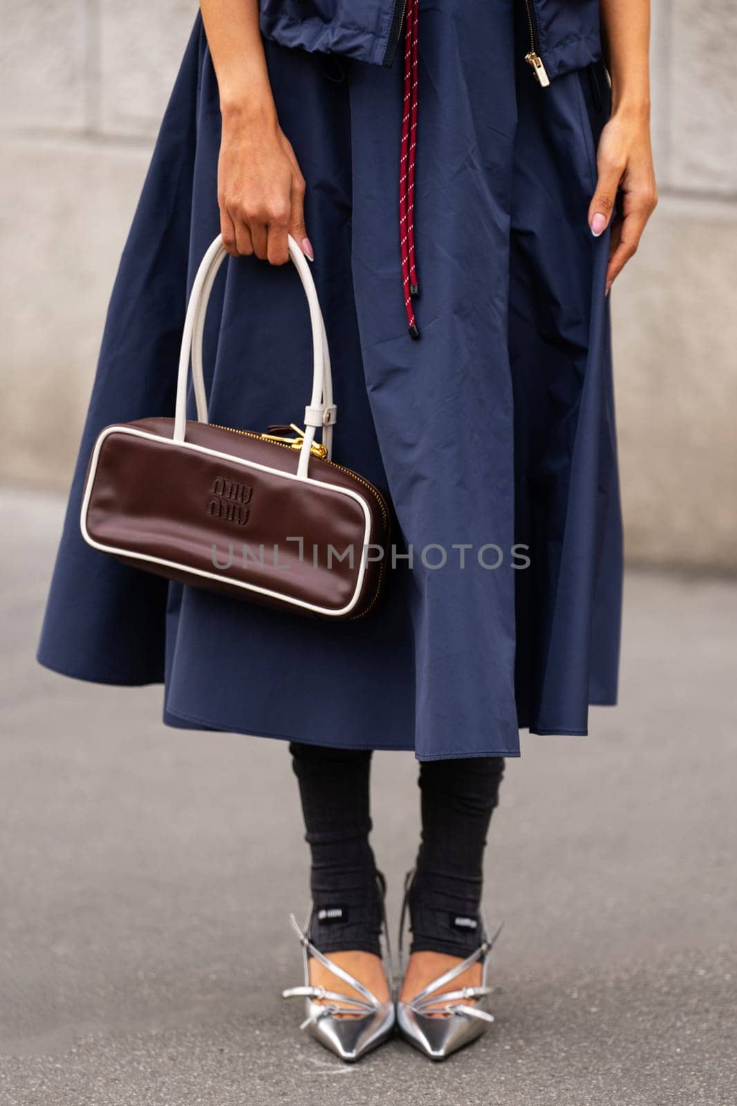 Paris, France - March 11, 2025: Miu Miu brown leather top handle bag, navy skirt, silver spiked pointed pumps. Street style outfit details.