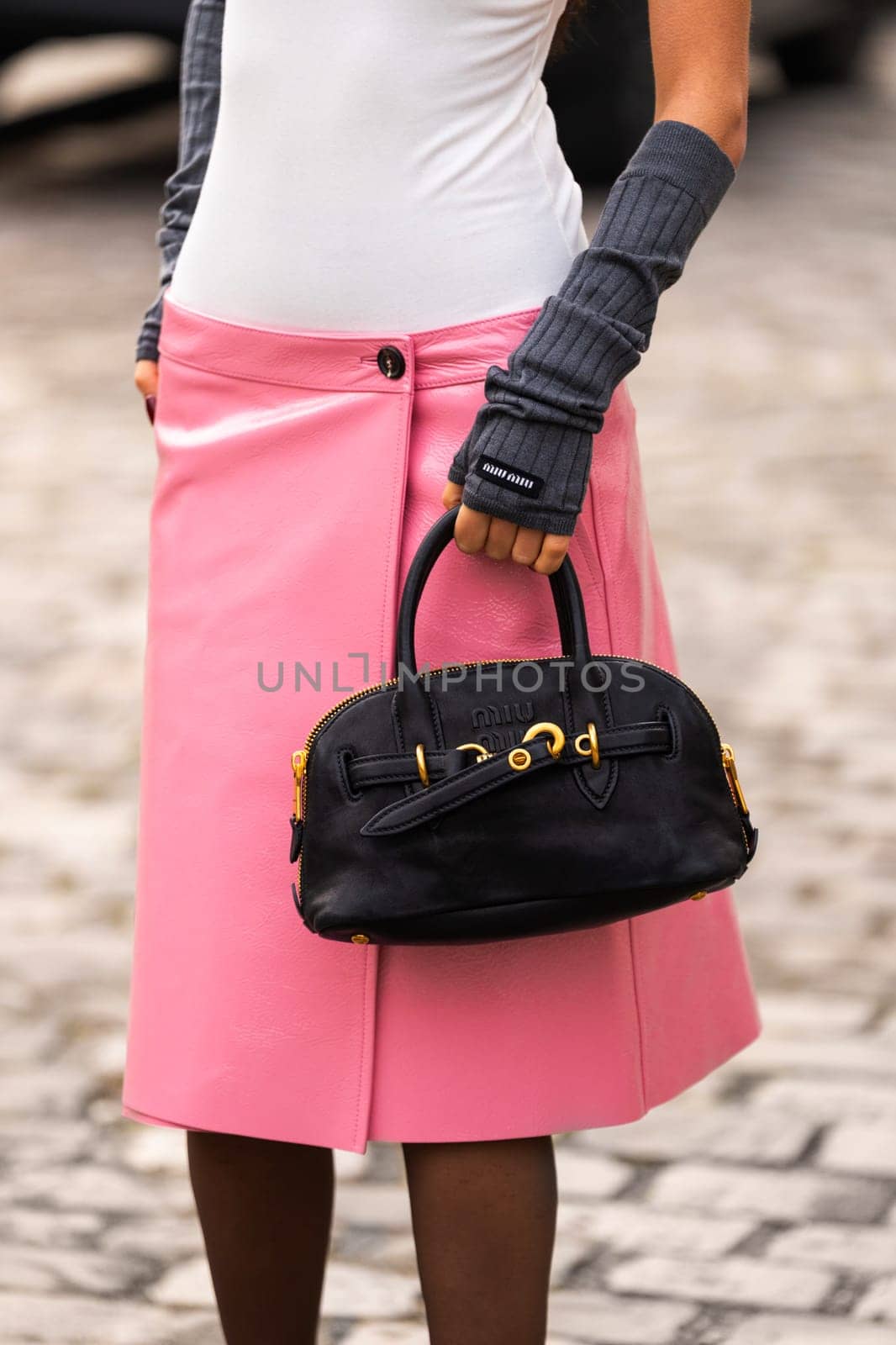 Paris, France - March 11, 2025: Woman wears black Miu Miu bag with gold hardware and top handles, styled with pink vinyl textured skirt. Street style outfit details.
