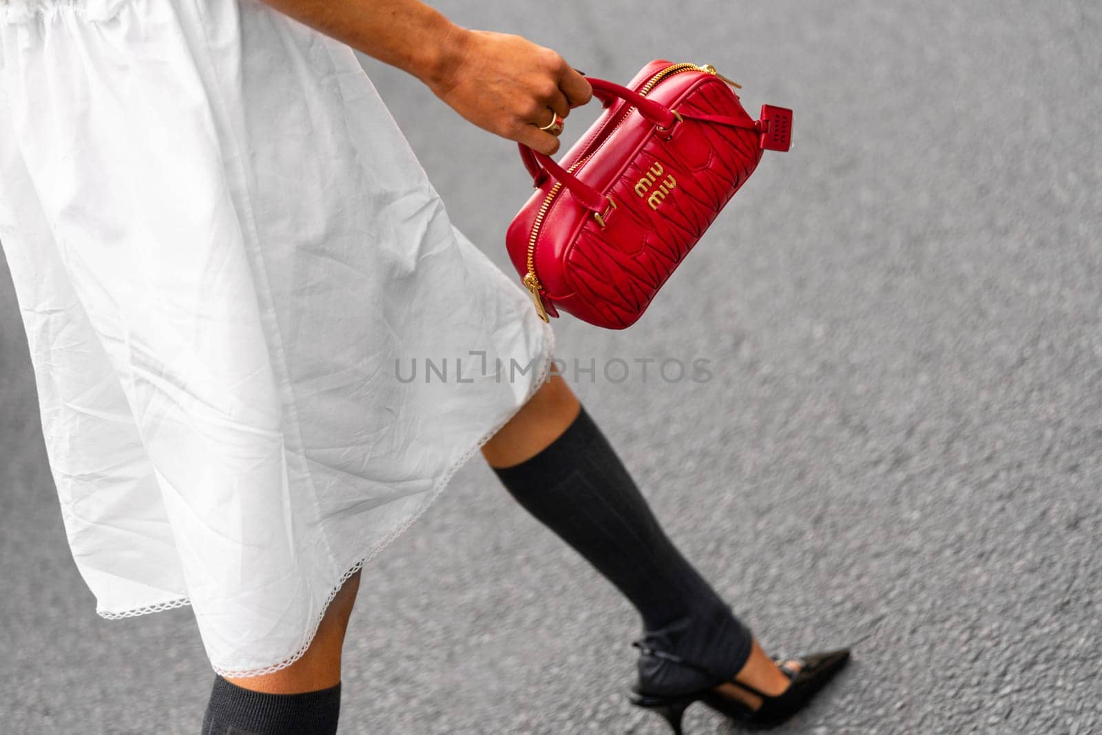 Paris, France - March 11, 2025: Woman wears red Miu Miu bag with gold logo and quilted leather, styled with white slip dress and black kitten heels. Street style outfit details.