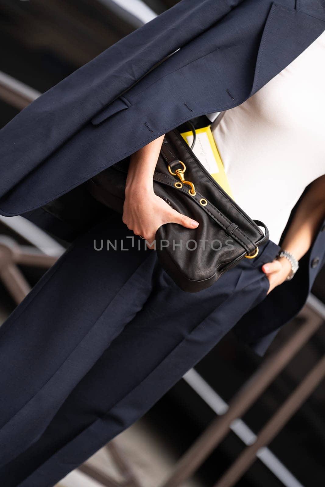 Paris, France - March 11, 2025: Woman wears black Miu Miu clutch bag with gold clasp hardware and yellow envelope. Street style outfit details.