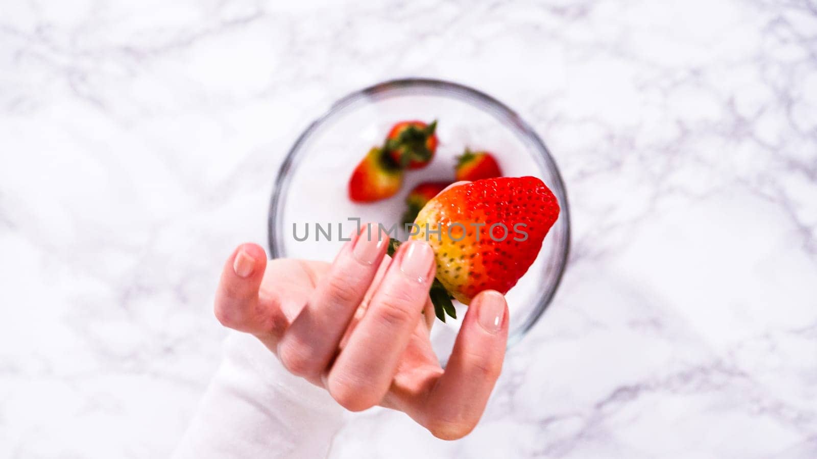 Flat lay. Strawberries, freshly washed and dried, are neatly stored in a glass bowl lined with a paper towel and securely covered with plastic wrap to maintain freshness.