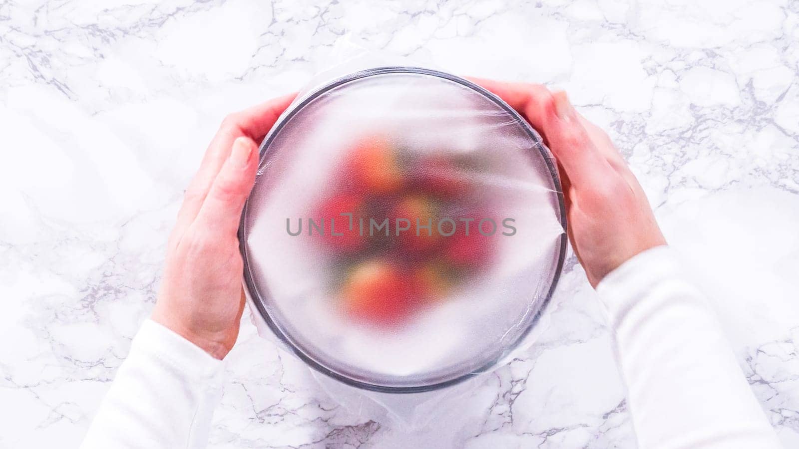 Flat lay. Strawberries, freshly washed and dried, are neatly stored in a glass bowl lined with a paper towel and securely covered with plastic wrap to maintain freshness.