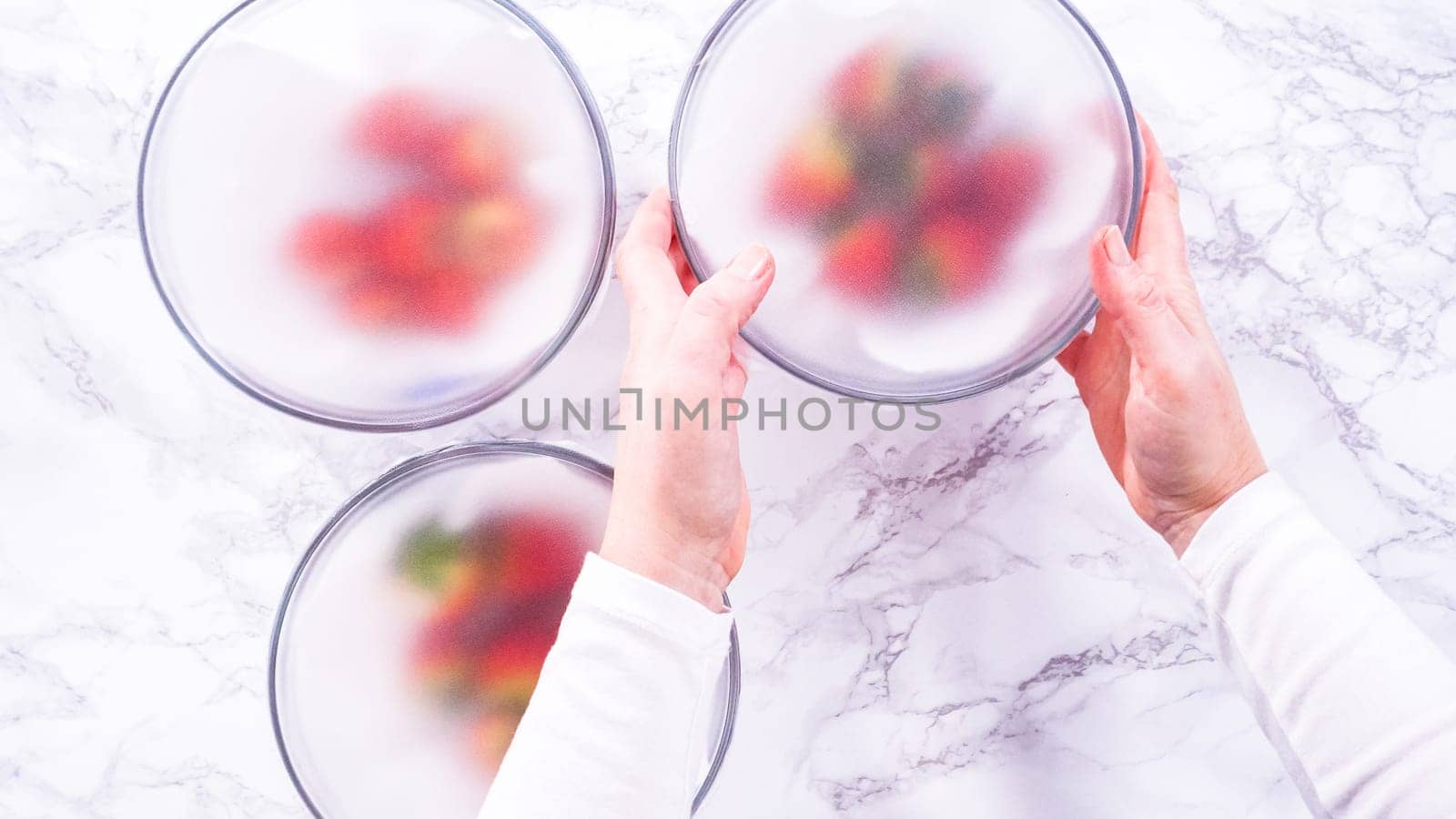 Flat lay. Strawberries, freshly washed and dried, are neatly stored in a glass bowl lined with a paper towel and securely covered with plastic wrap to maintain freshness.