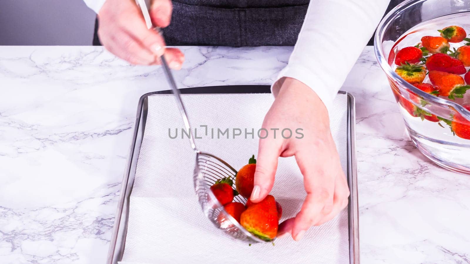 Juicy red strawberries, freshly washed, are spread out to dry on a baking sheet, carefully lined with paper towels to absorb excess moisture and prevent mold.